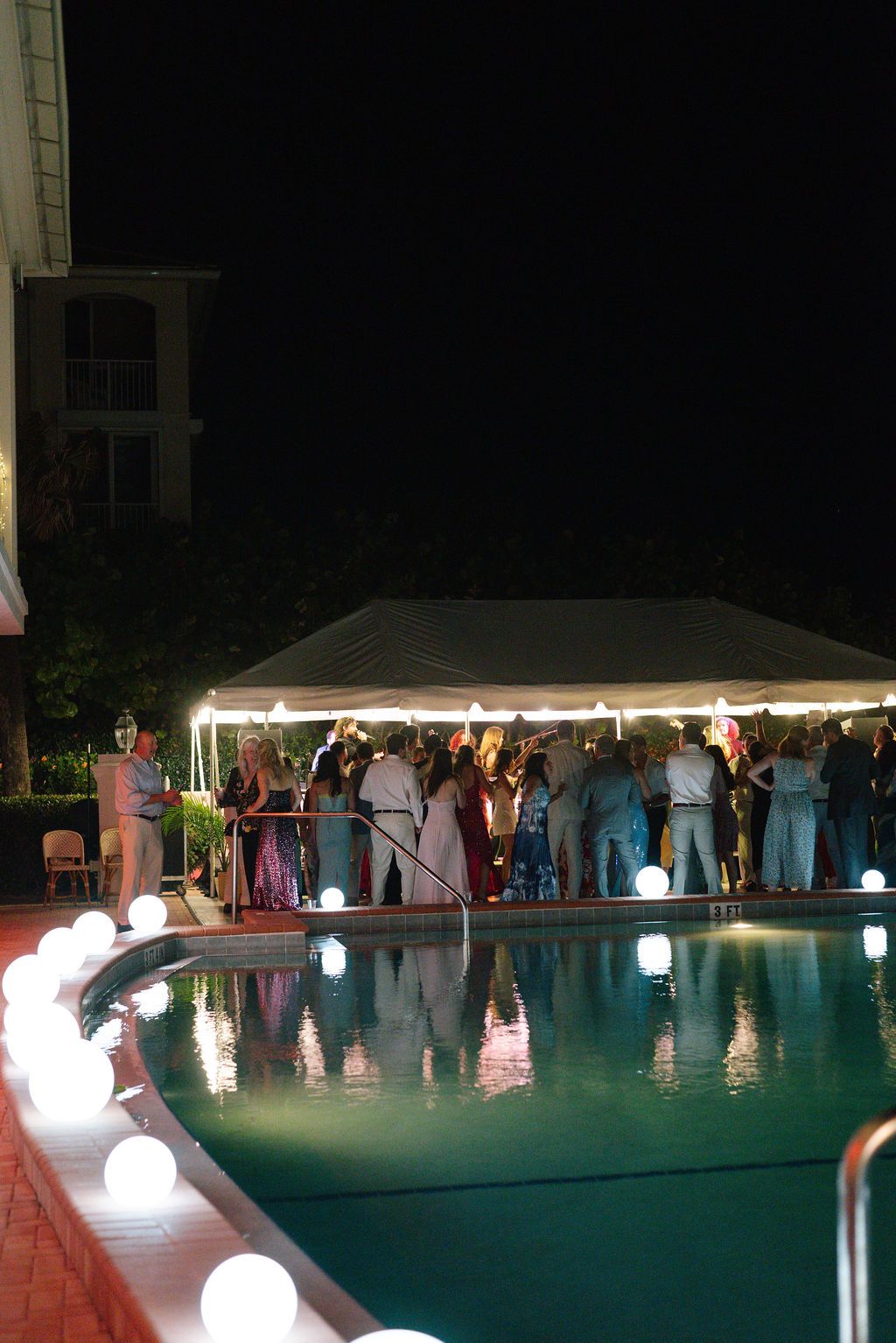 Nighttime poolside party scene with glowing orb lights and guests gathered under a white tent.