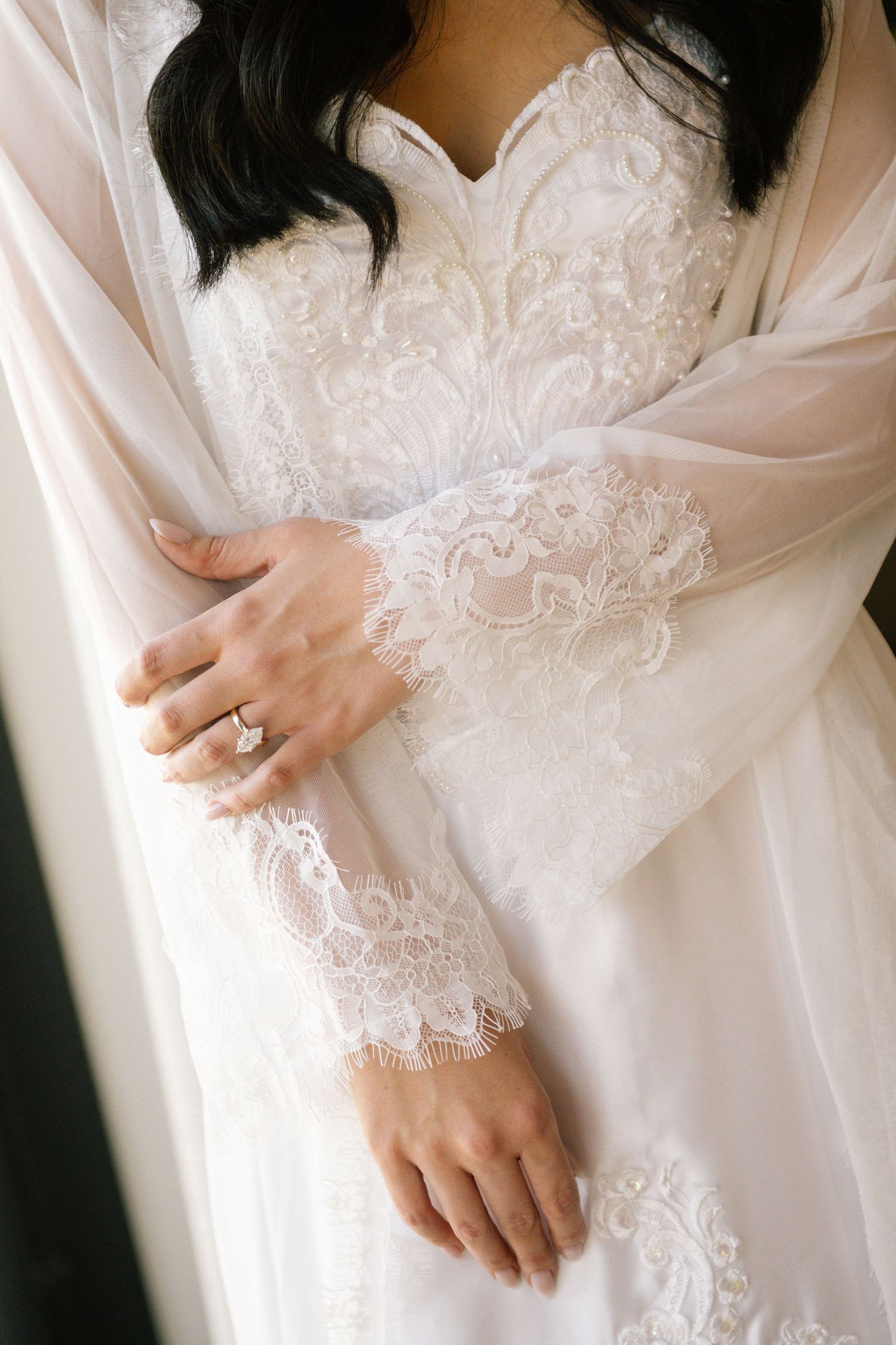Close-up of lace detail on white bridal robe with engagement ring.