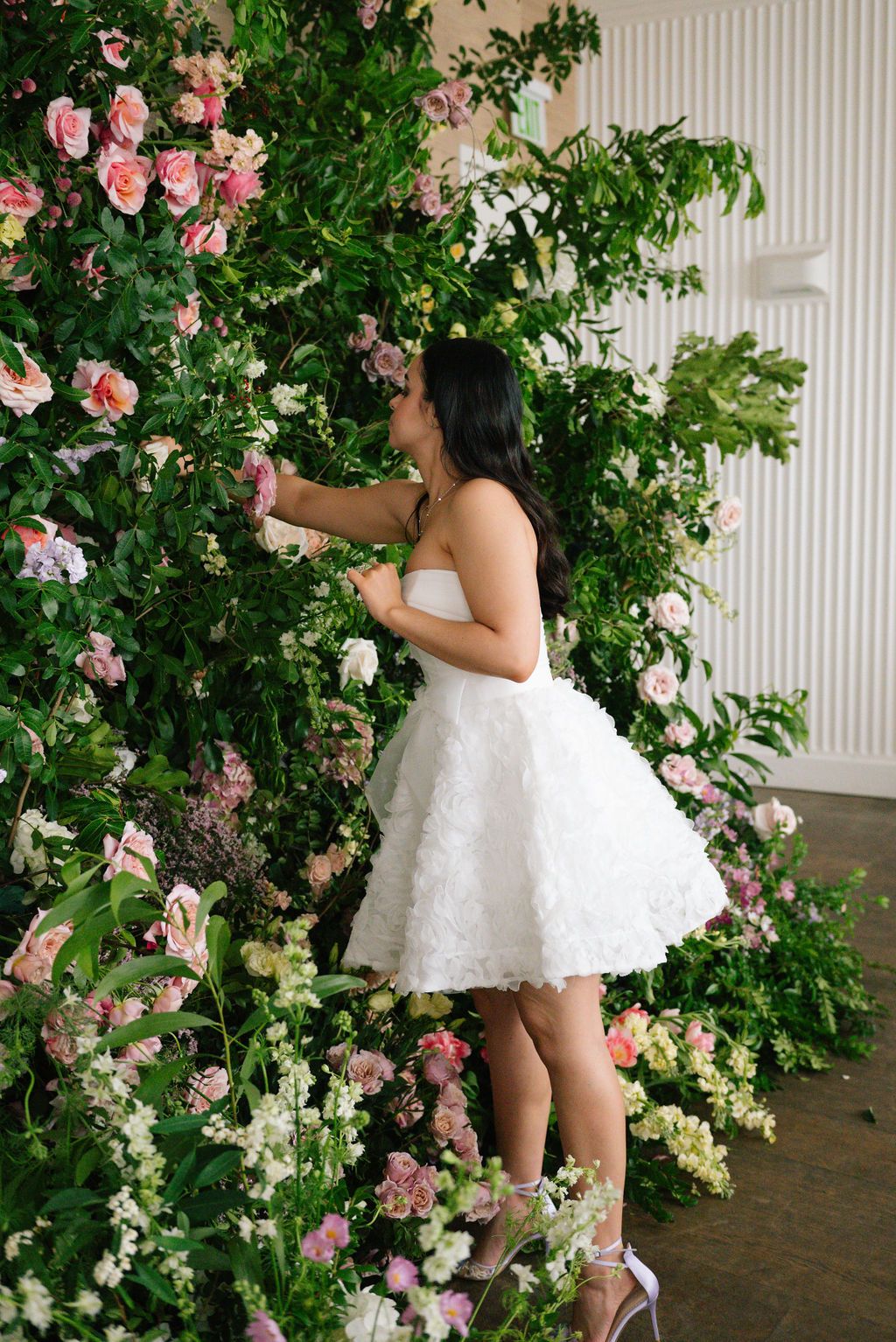 White dress against lush garden backdrop with pink and cream roses.