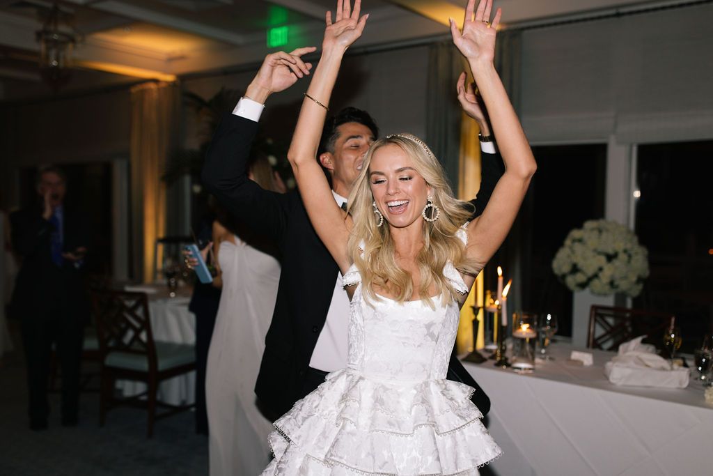 A bride dances joyfully at her reception in a white ruffled dress.