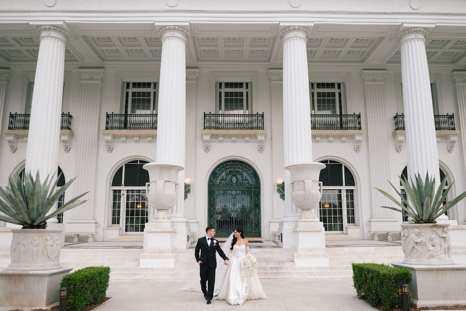 A wedding scene captured along a grand white colonnade with classic architectural details.