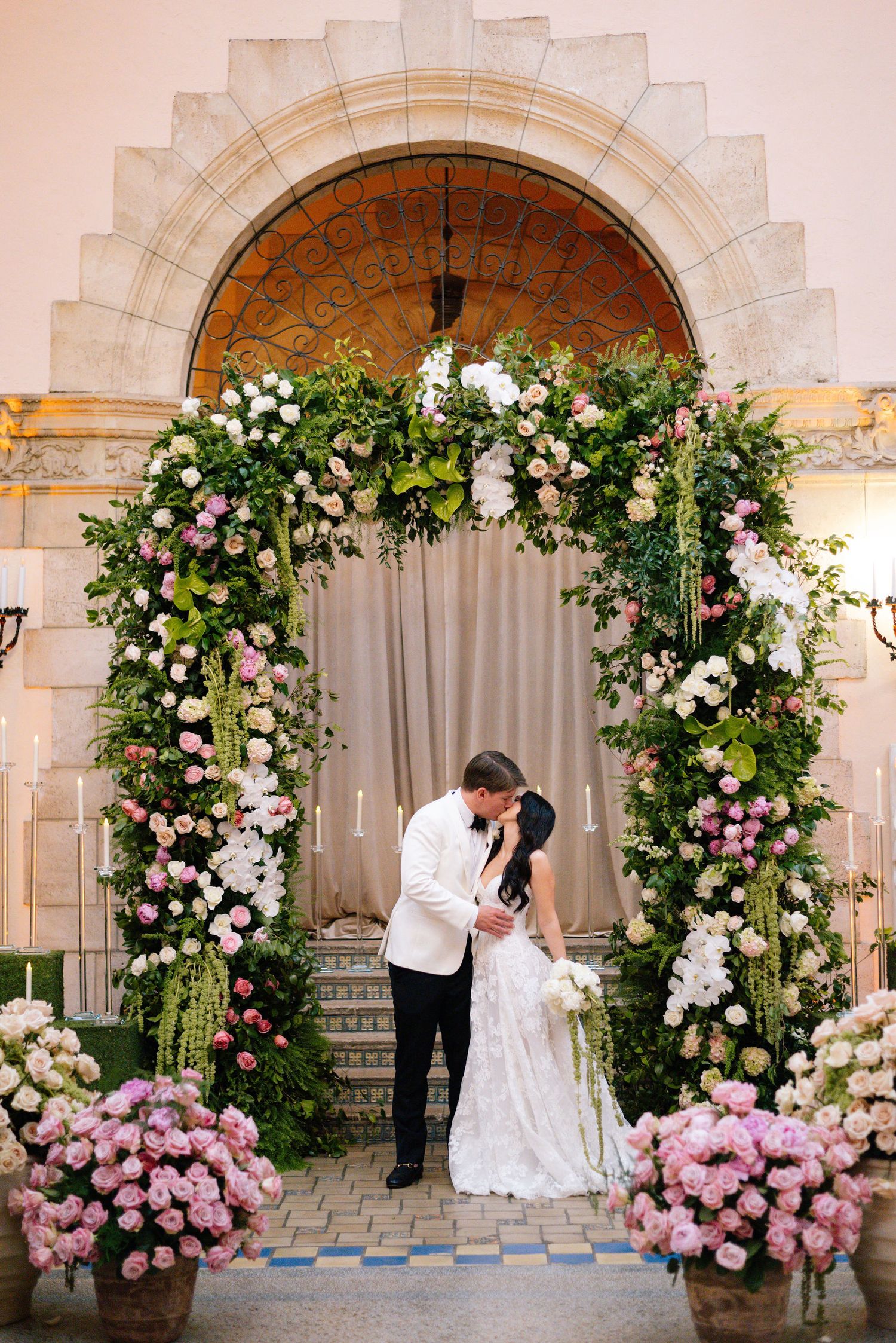 Romantic stone archway decorated with climbing roses and flowers for a wedding ceremony.