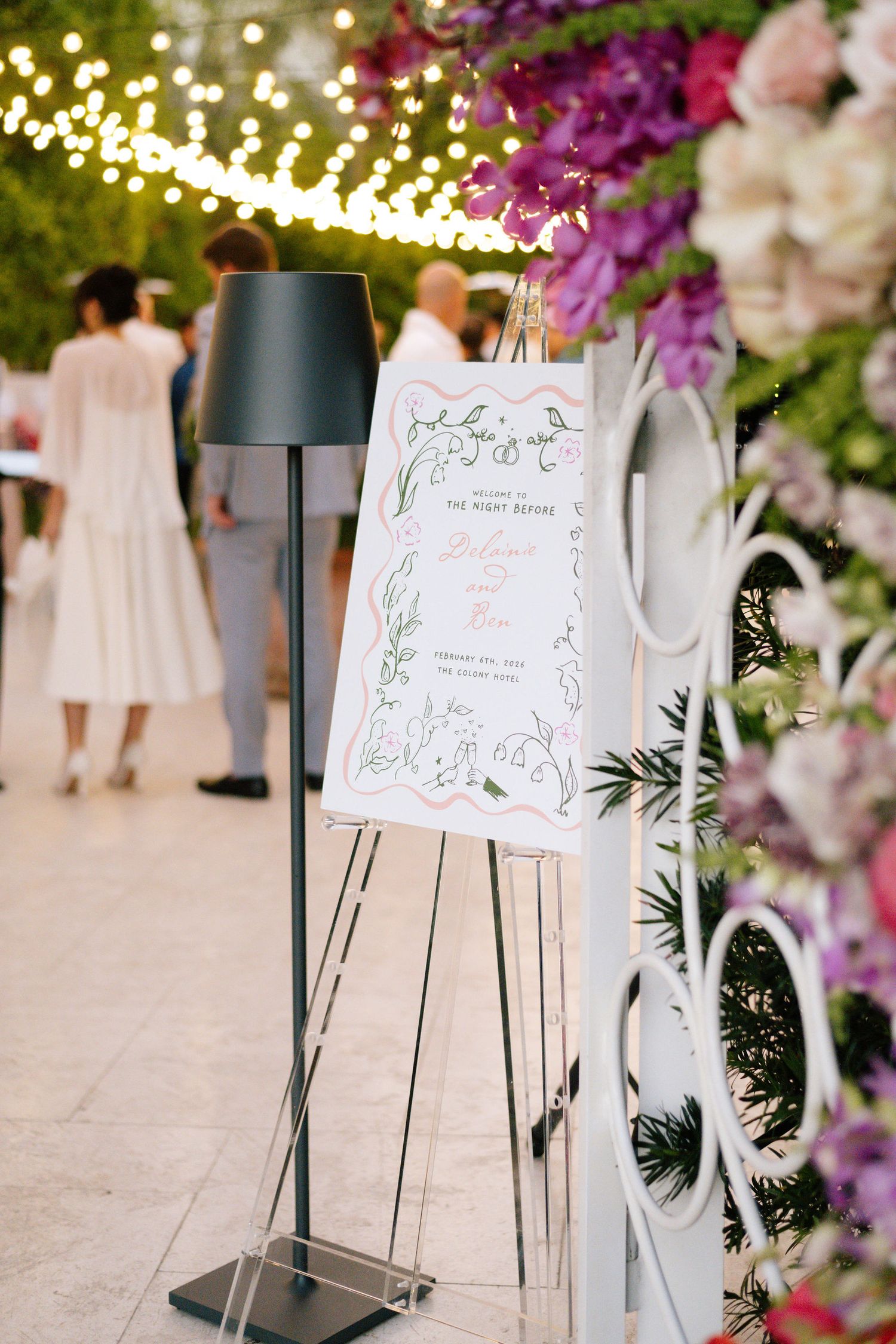 Wedding seating chart signs displayed with purple floral decorations and string lights.