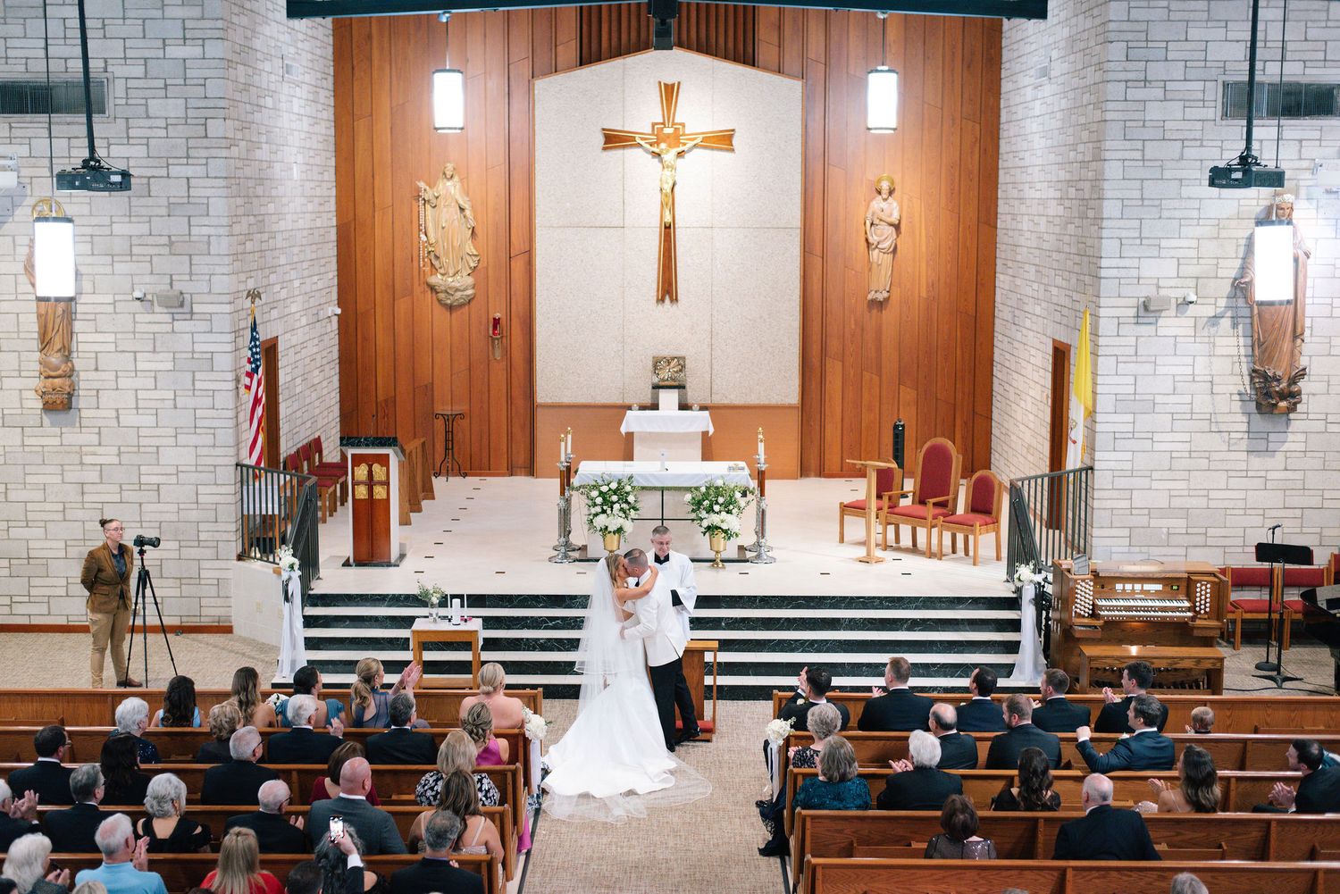 A traditional Catholic church interior with wooden pews, brick walls, and a crucifix displayed at the altar during a ceremony.