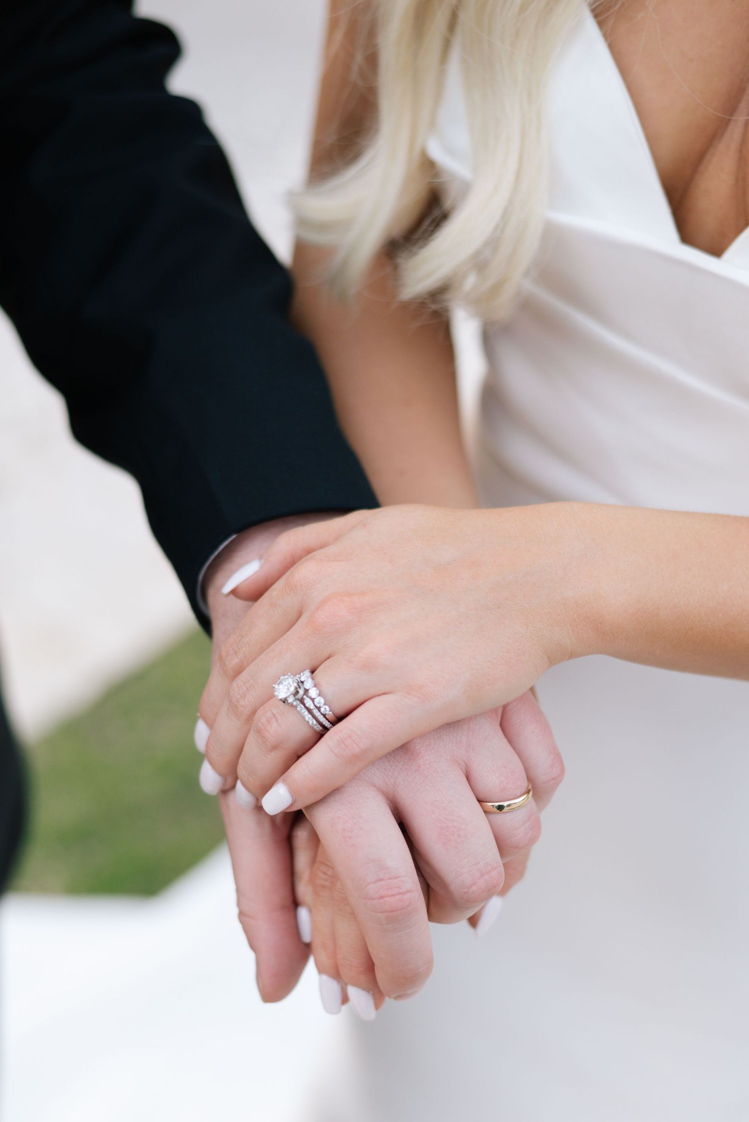 Close-up shots of hands with wedding rings and white manicured nails holding each other.
