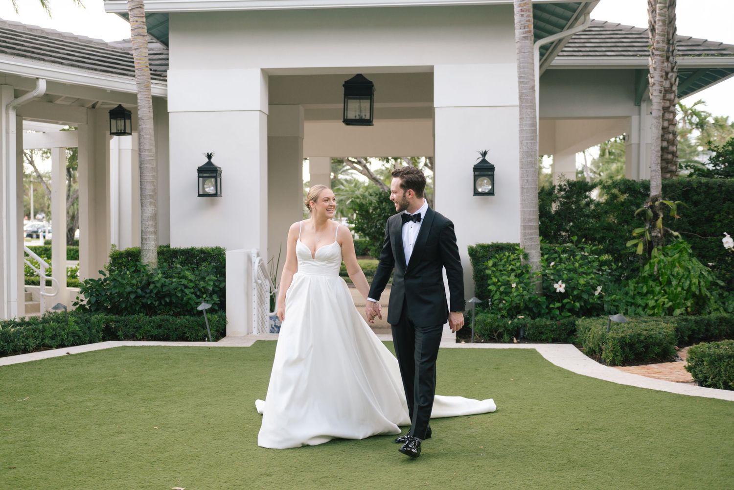 A couple walks together on a manicured lawn in front of an elegant white columned building entrance.