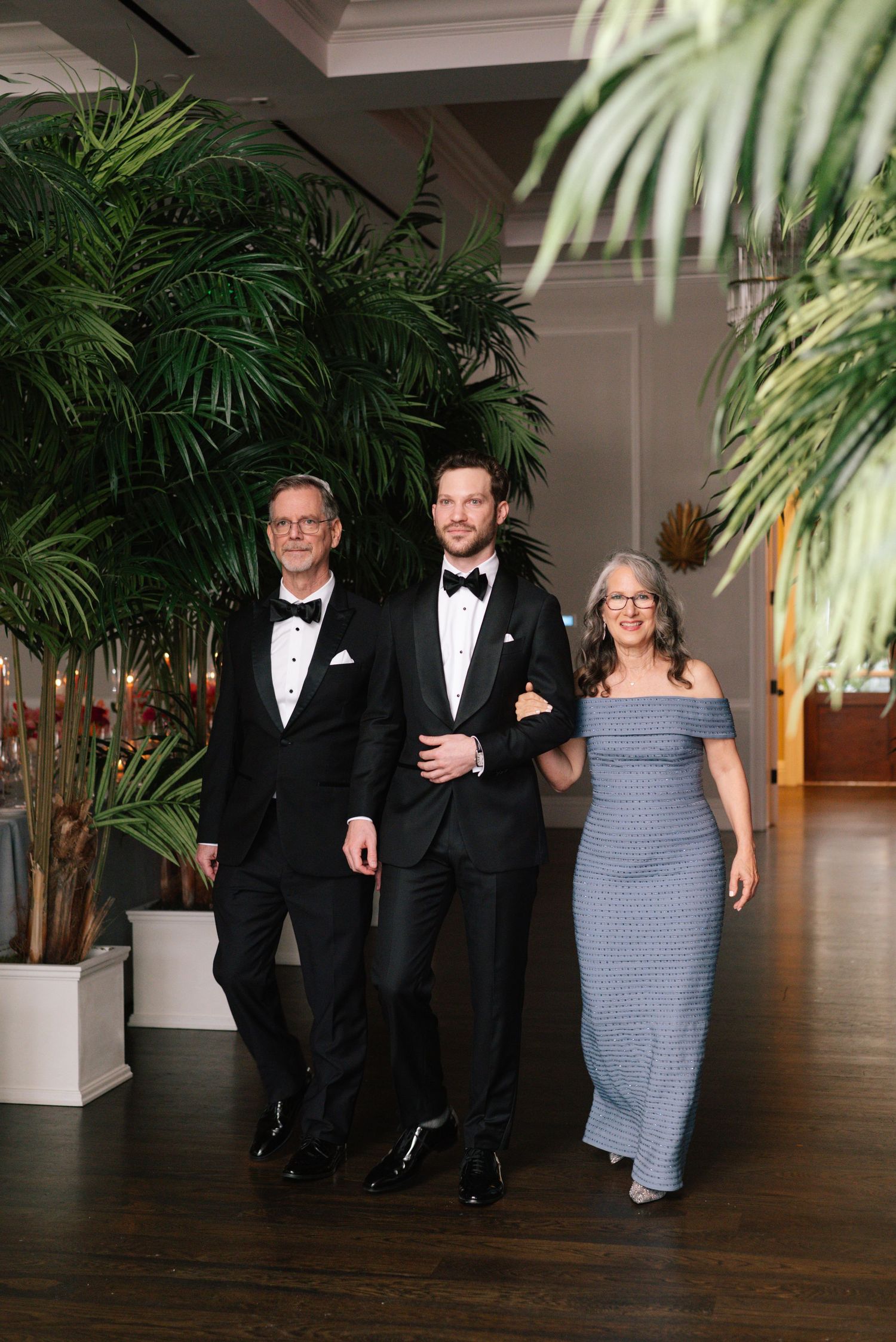 Wedding party members walking down a tropical-themed hallway with indoor palm trees.