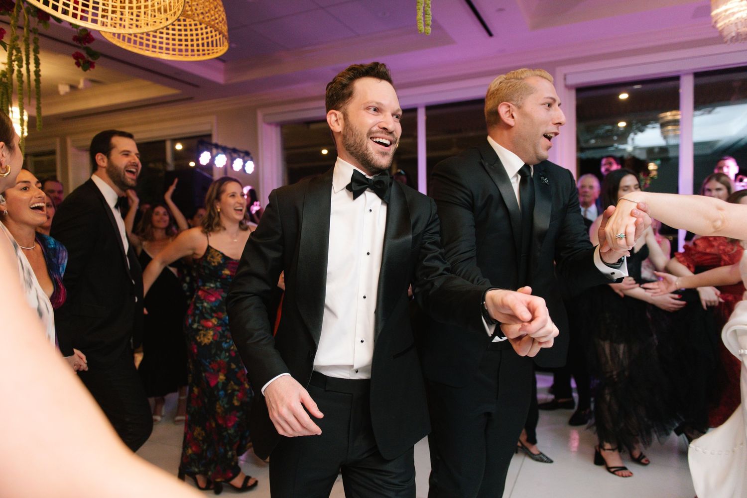 Wedding guests dancing and celebrating on an illuminated dance floor.