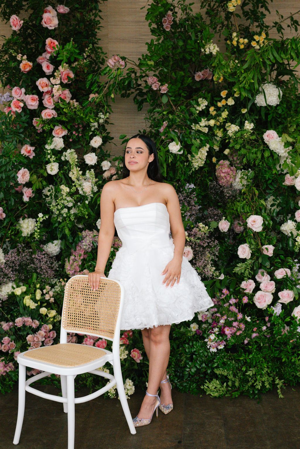 Wedding photos with a white cane chair against a wall of climbing roses and greenery.