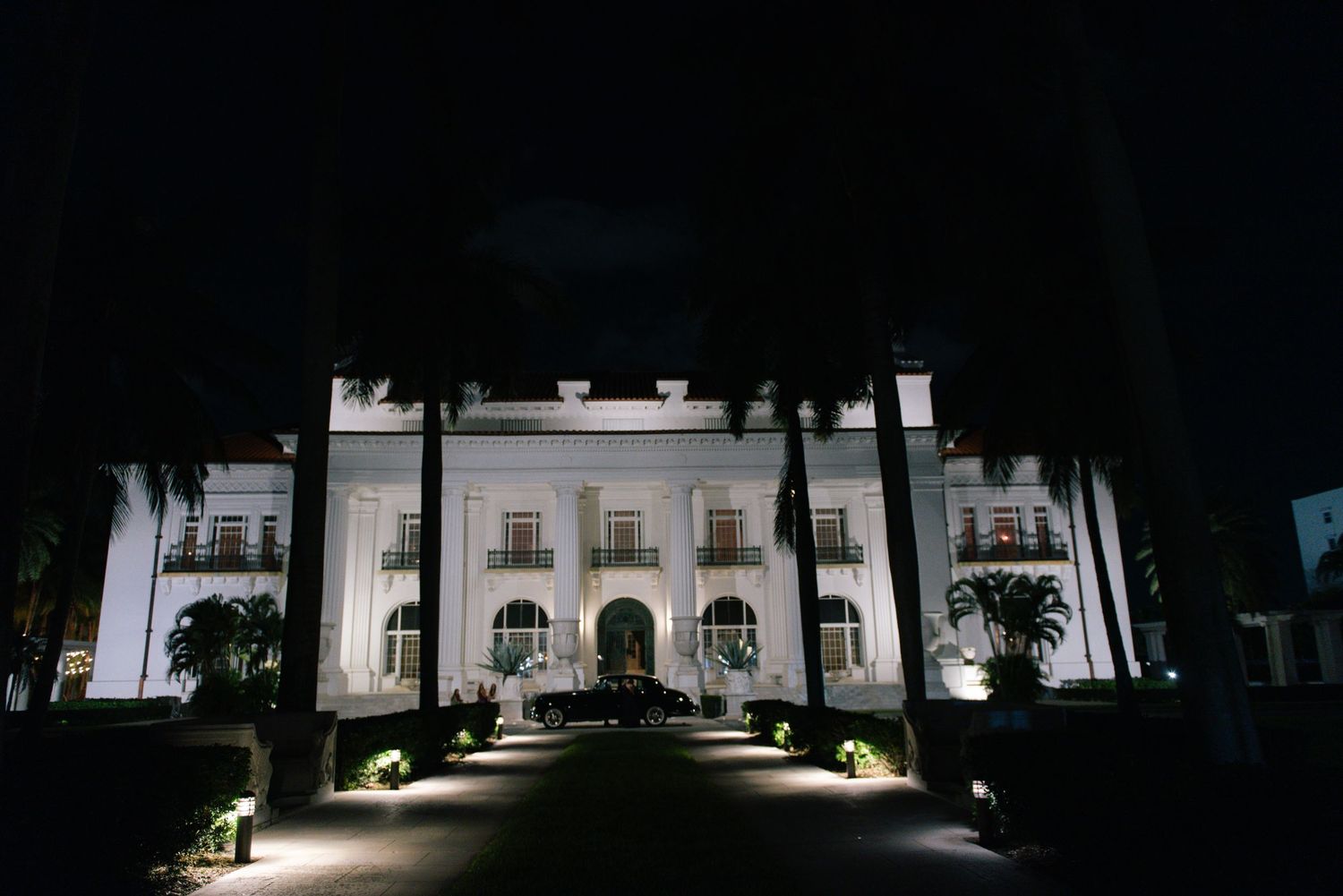 Grand white mansion wedding venue illuminated at night surrounded by palm trees.