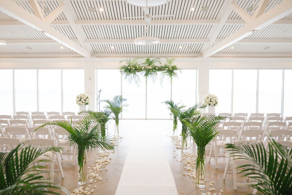 Clean white wedding venue with vaulted ceilings and tropical greenery arrangements.