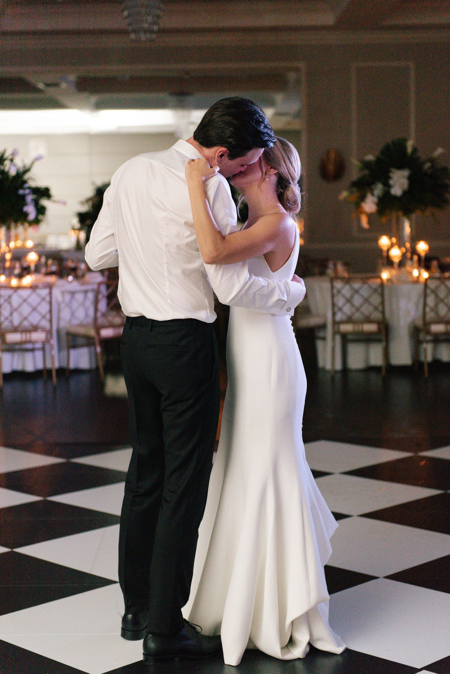 Newlyweds dancing together on a striking black and white checkered dance floor at their reception.