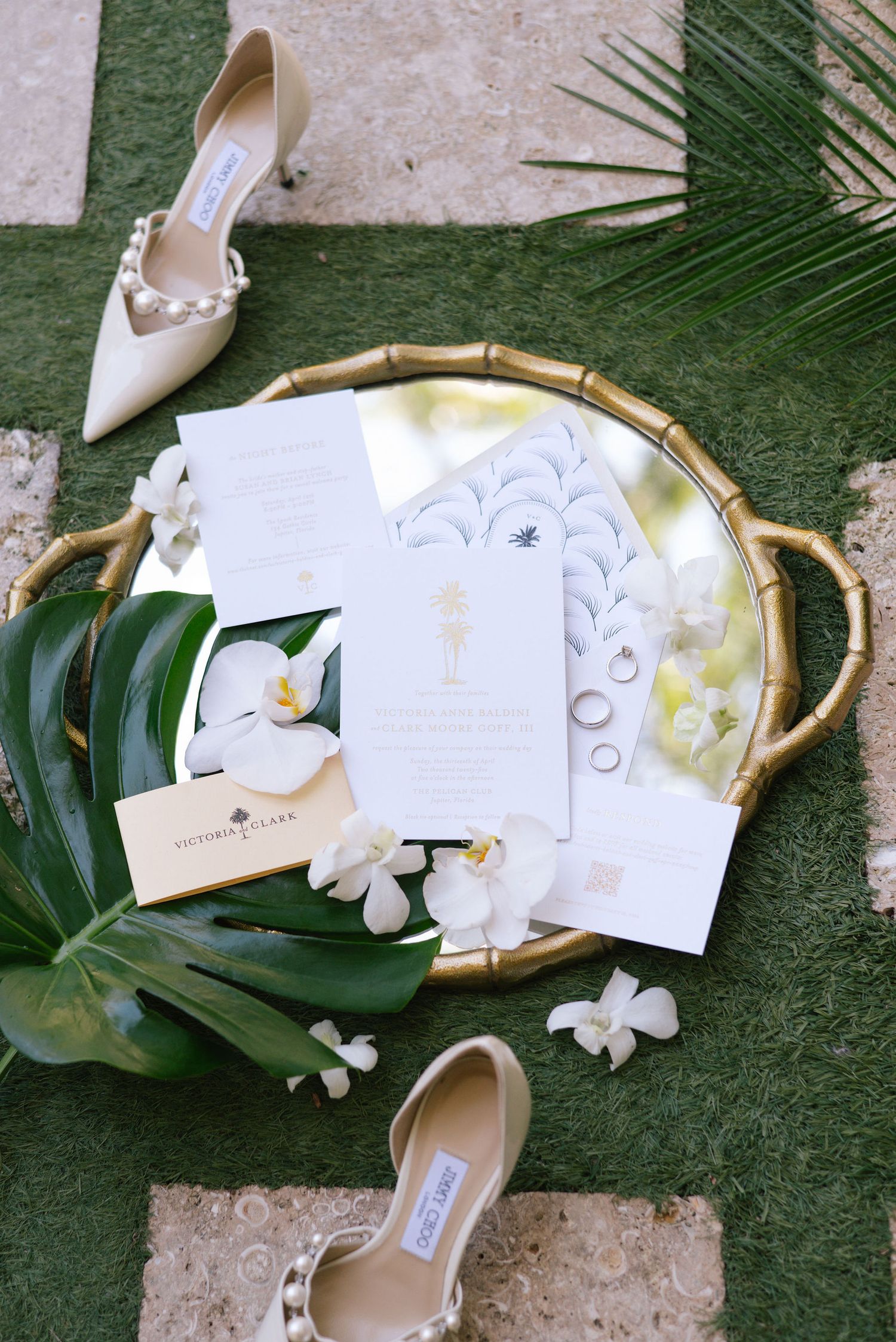 Wedding details with white orchids, tropical leaves, and elegant stationery arranged on a textured surface.
