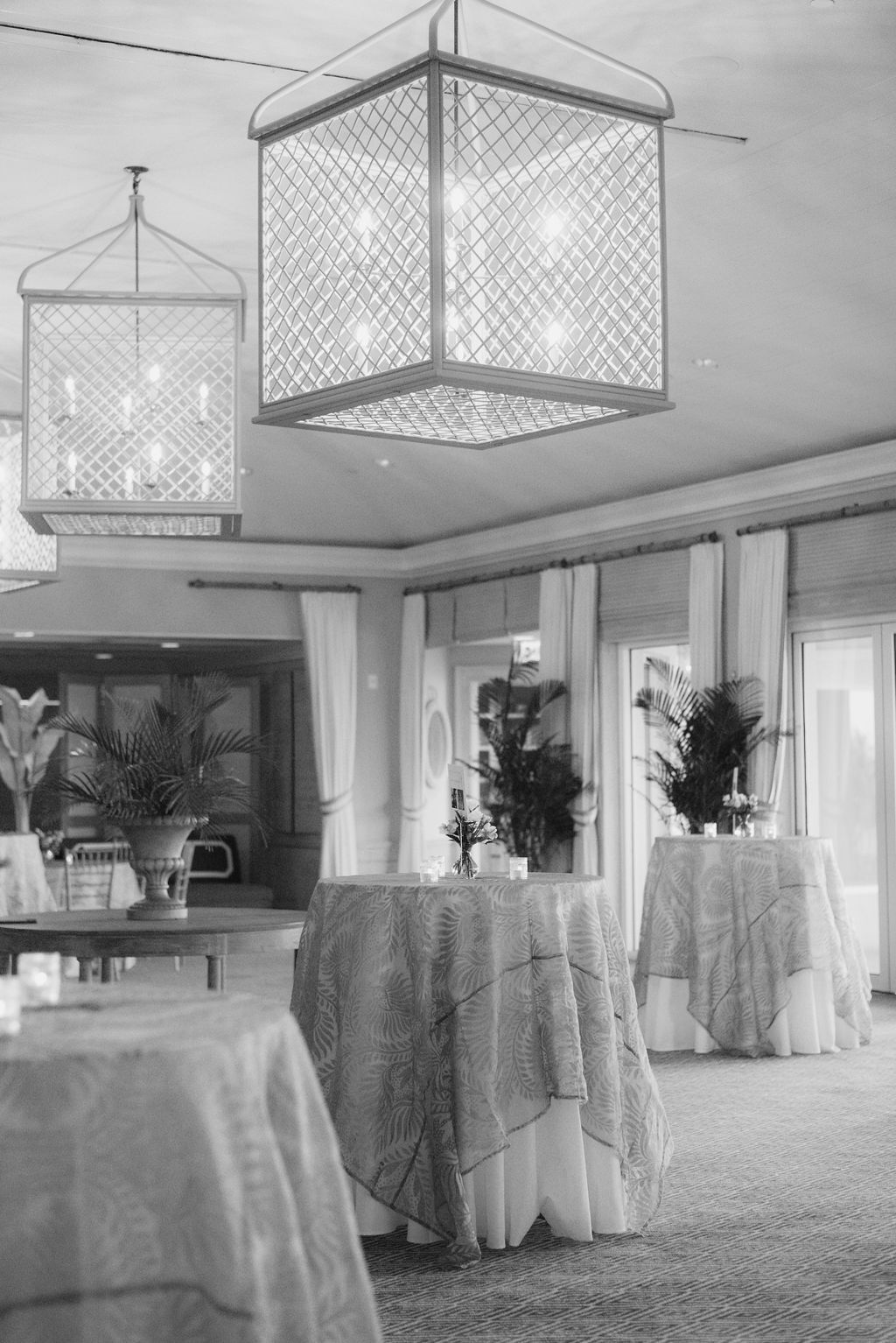 Black and white photo of a banquet room with modern pendant lighting and round tables.