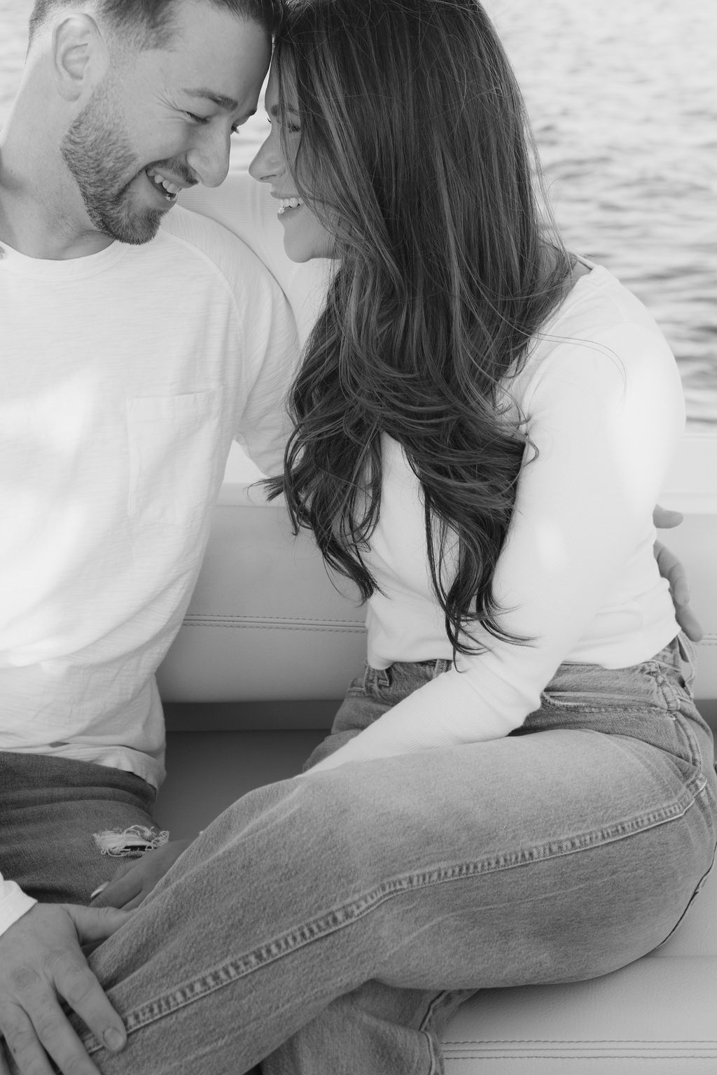 Black and white photo of couple sharing intimate moment on boat seating.