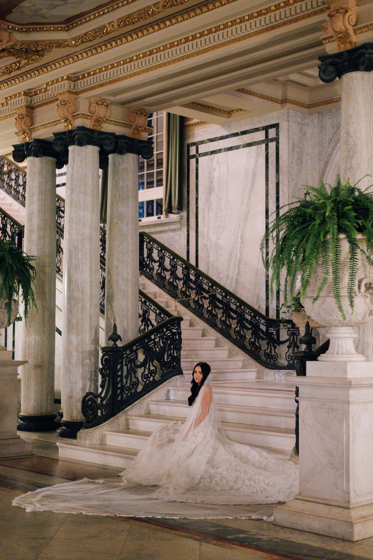 Dramatic bridal portraits on grand staircase with ornate railings and hanging plants.