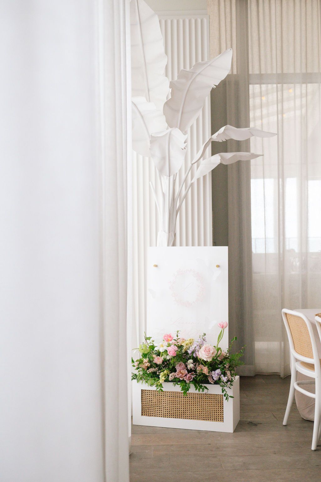 Elegant white event space with sheer curtains and floral arrangements along window ledges.