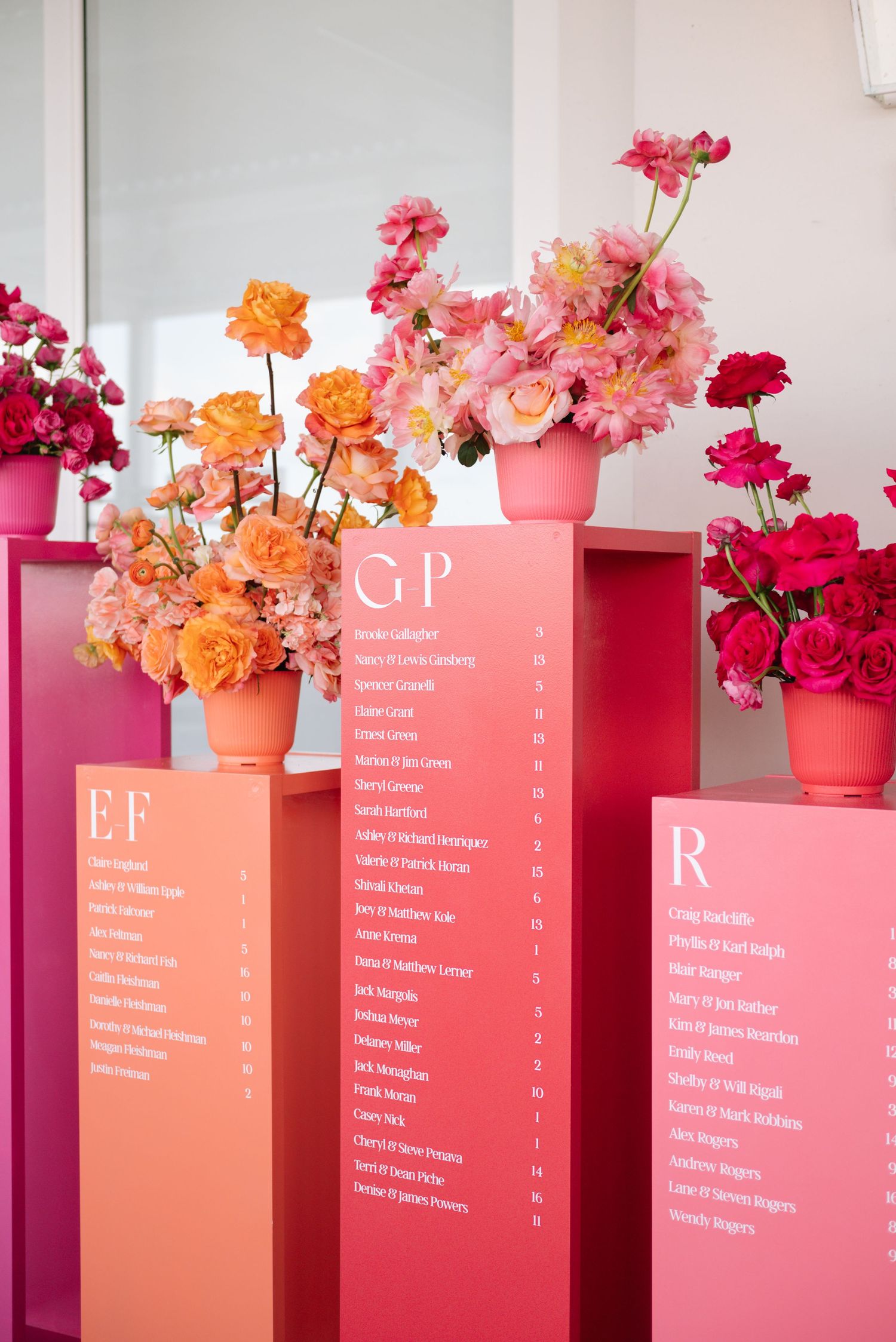 Pink and coral seating chart displays with colorful flower arrangements on top.