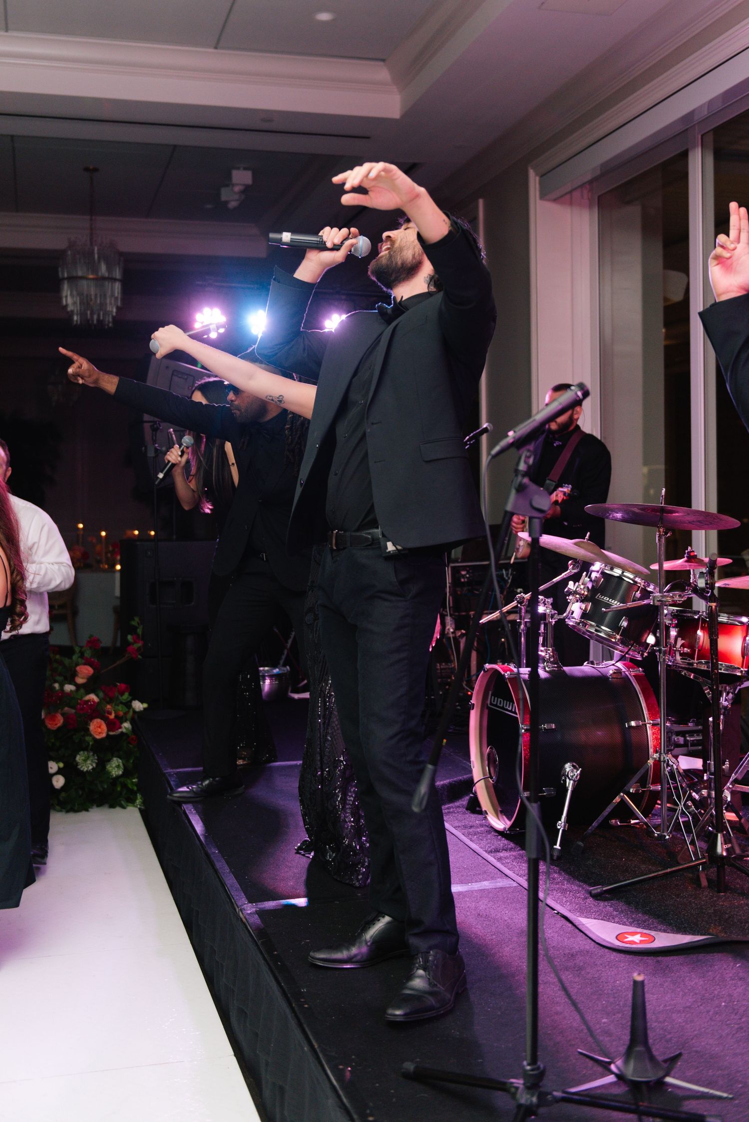 Live band performer on stage at wedding reception with drum kit visible in background.