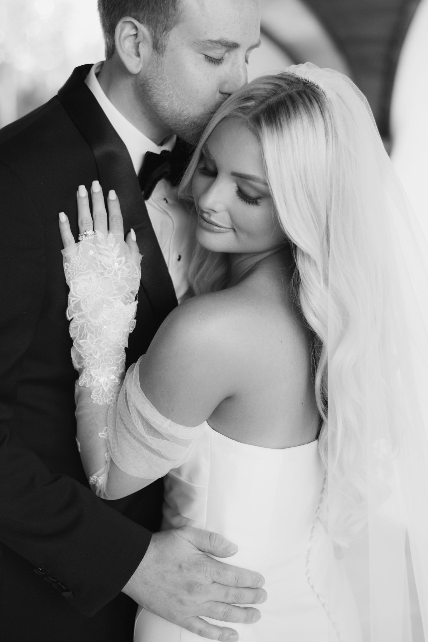 Black and white intimate portrait of newlyweds embracing, with bride wearing lace gloves and veil.