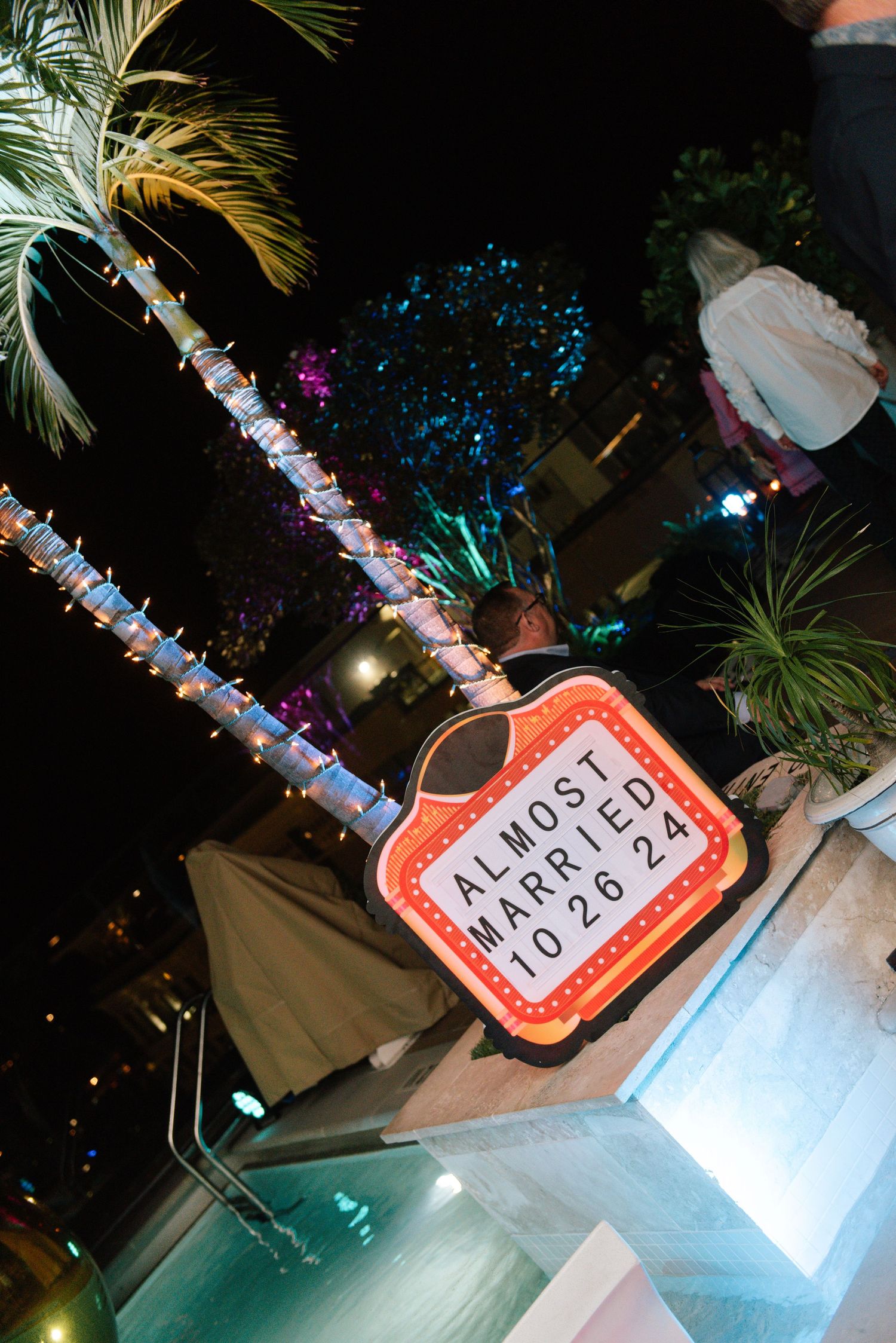Illuminated event signage with palm fronds and decorative lighting creating a tropical atmosphere.