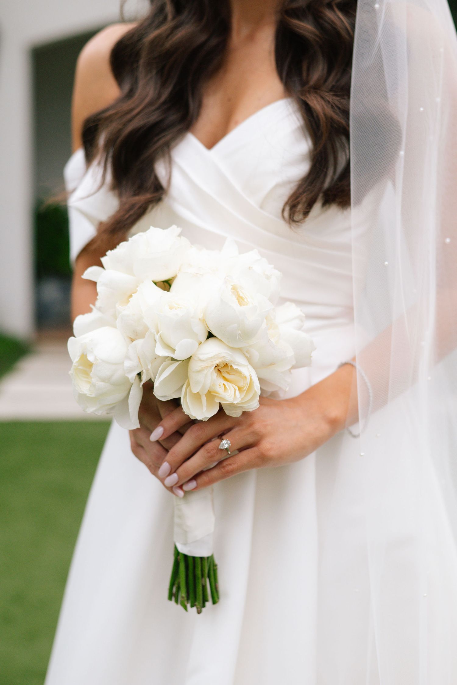 Close-up of white wedding bouquet with roses held by bride in white dress.