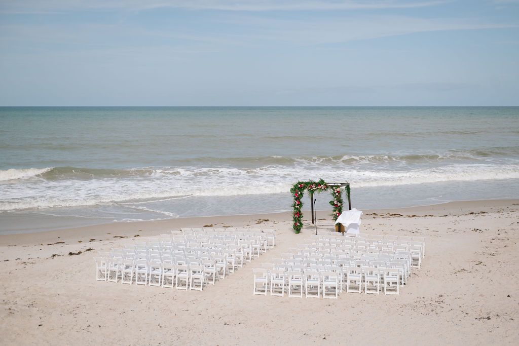 White chairs set up for a beach wedding ceremony with ocean views.