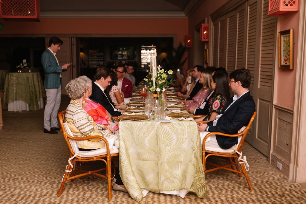 Formal dinner party with guests seated around elegantly decorated table with white linens.