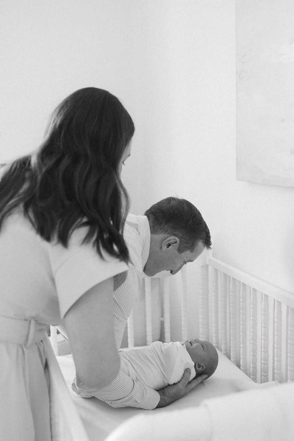 Two adults leaning over a white crib in a nursery setting.