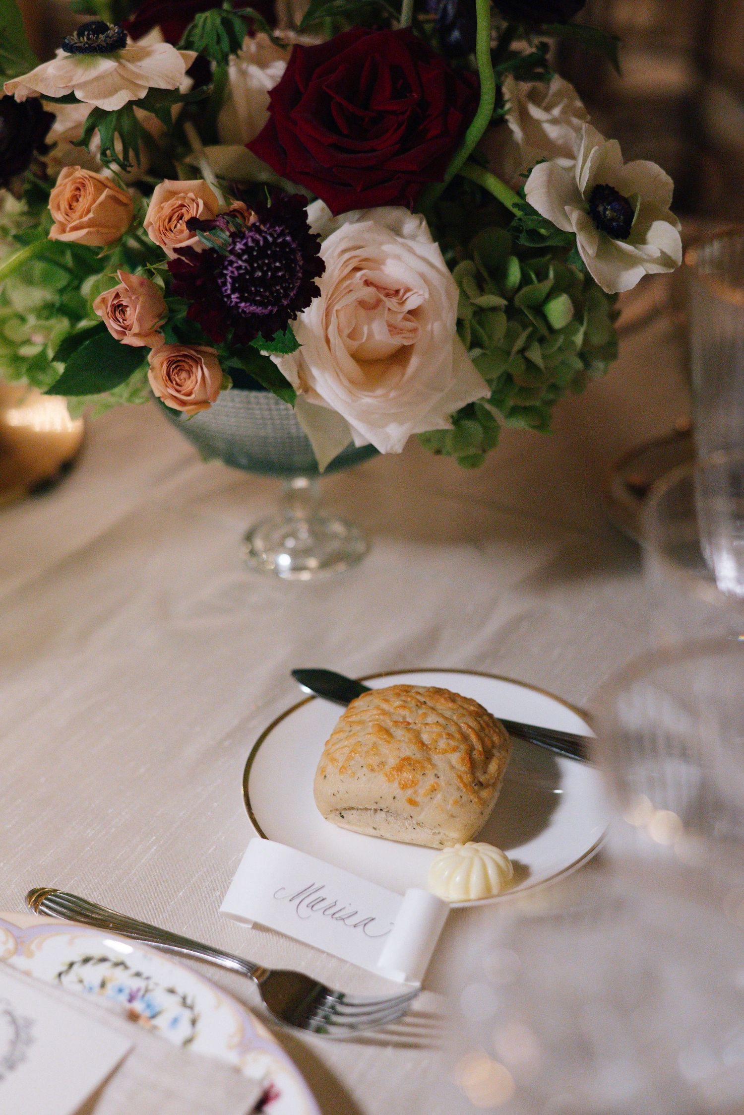 Close-up of wedding table setting with peach and burgundy floral centerpiece and bread roll on plate.