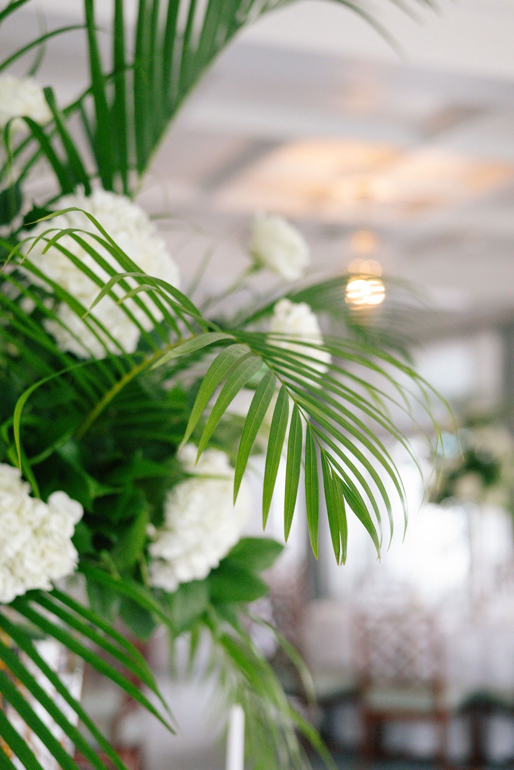Elegant tropical palm fronds and white floral arrangements create a romantic wedding reception ambiance.