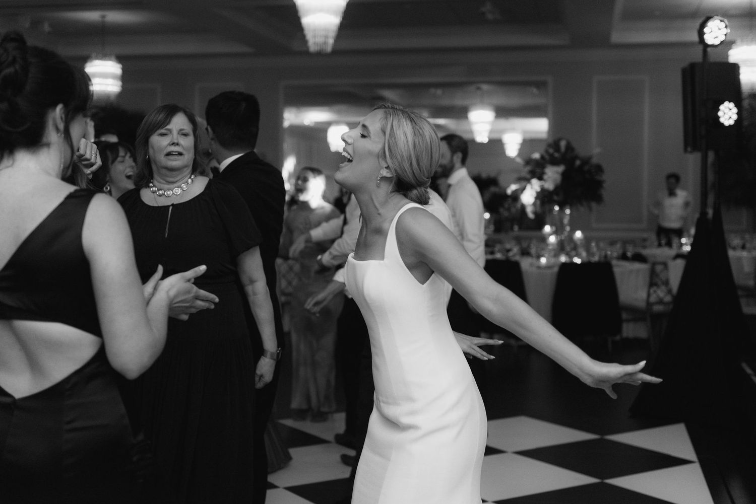 Wedding reception guests dancing and celebrating on a black and white checkered dance floor.