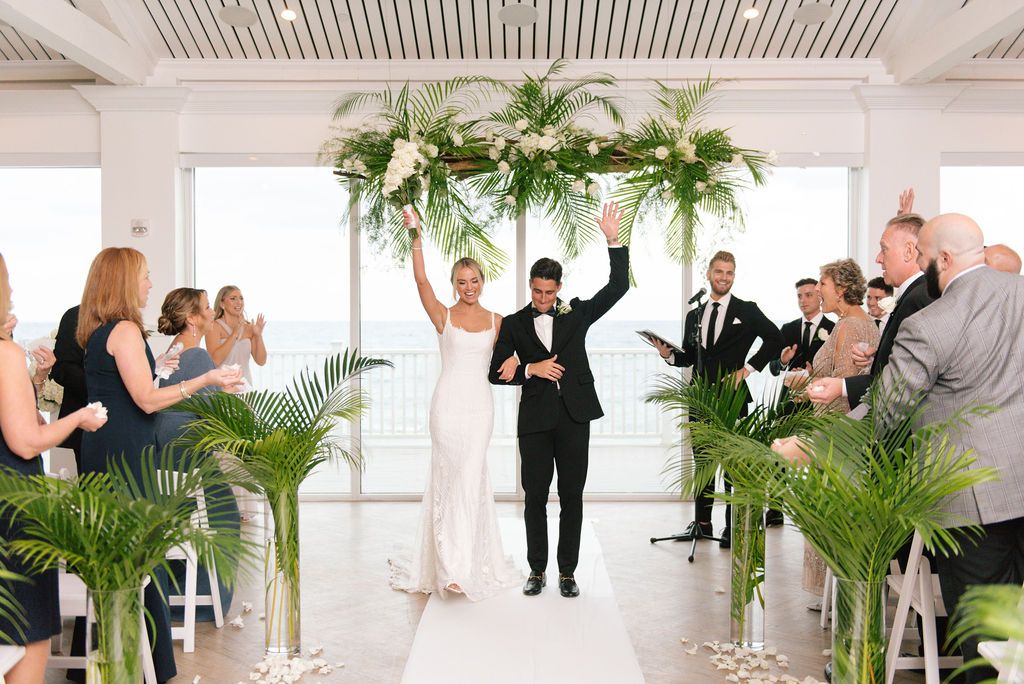 Joyful wedding recessional with guests clapping in bright coastal venue.