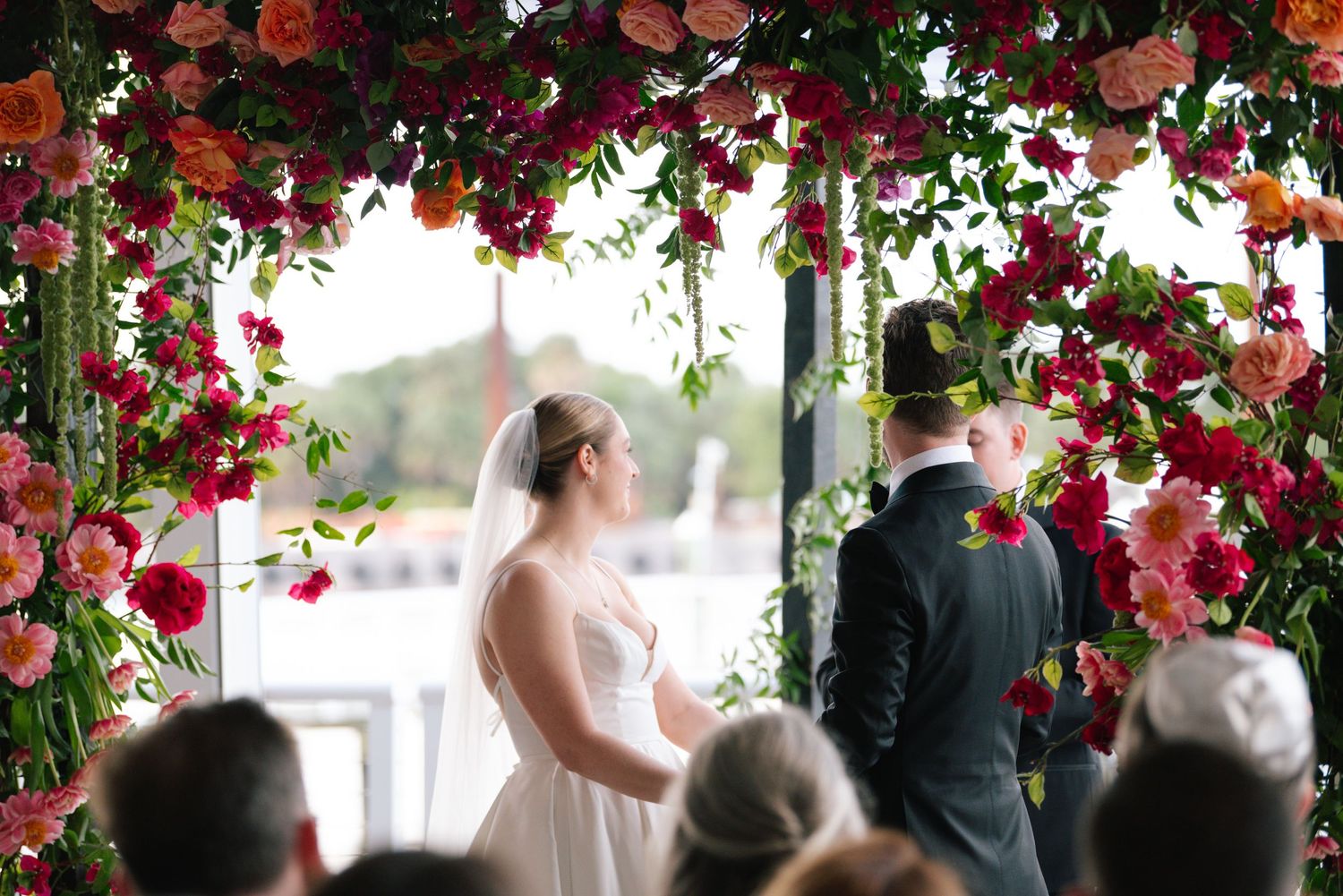 Wedding ceremony under lush floral arch with red and pink blooms.