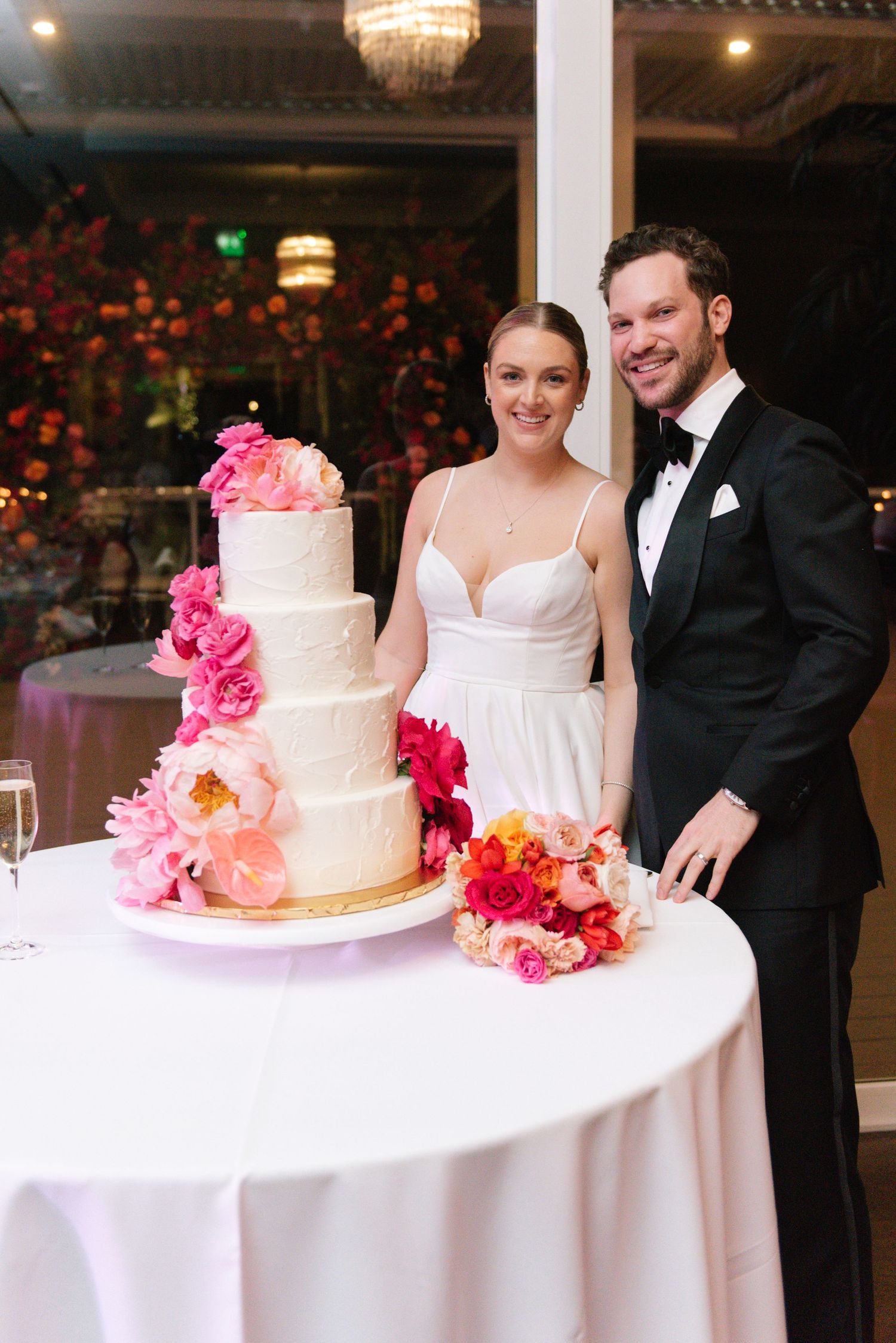 A white tiered wedding cake decorated with pink and coral flowers on display.