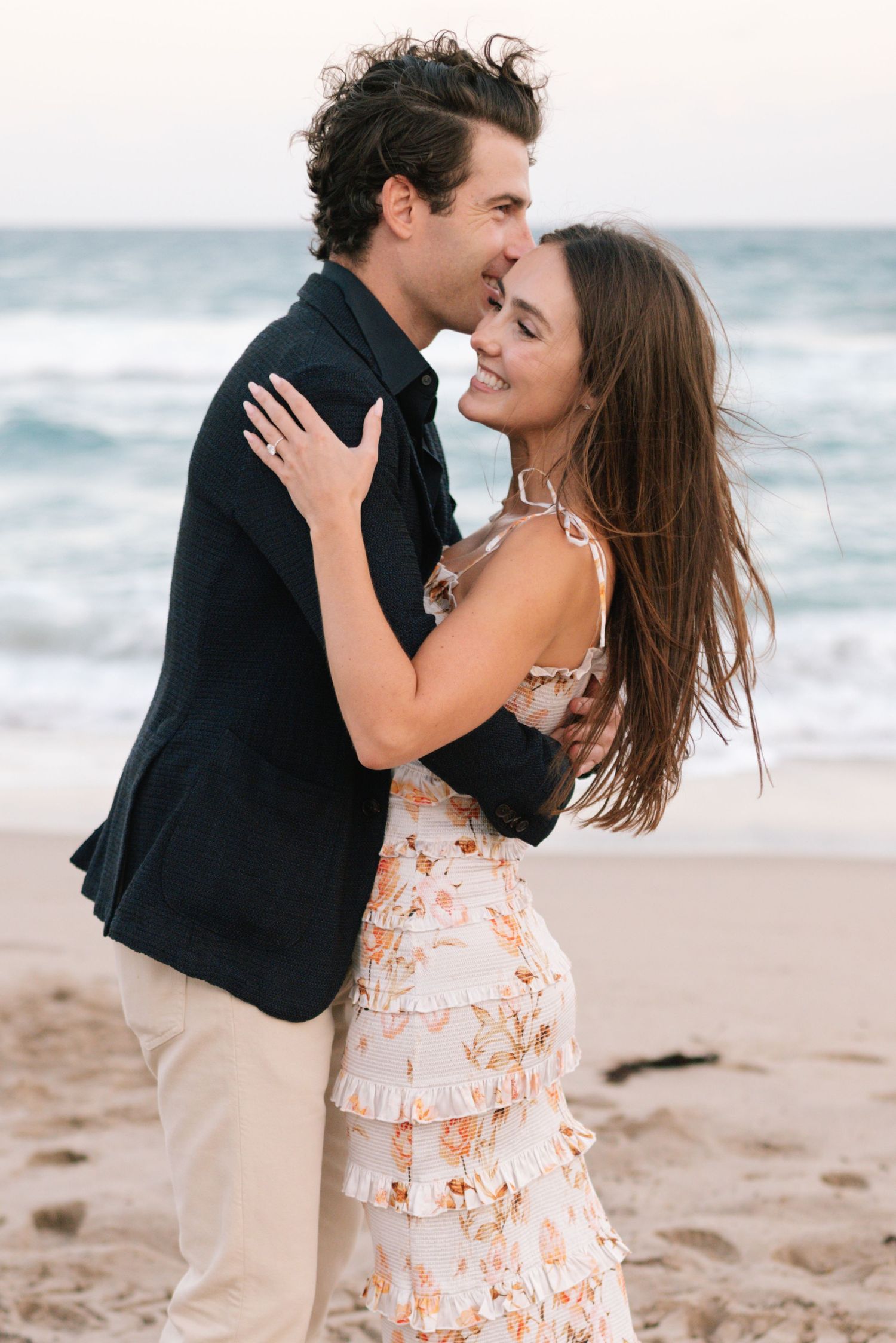 A couple shares romantic moments together on a sandy beach with ocean waves in the background.