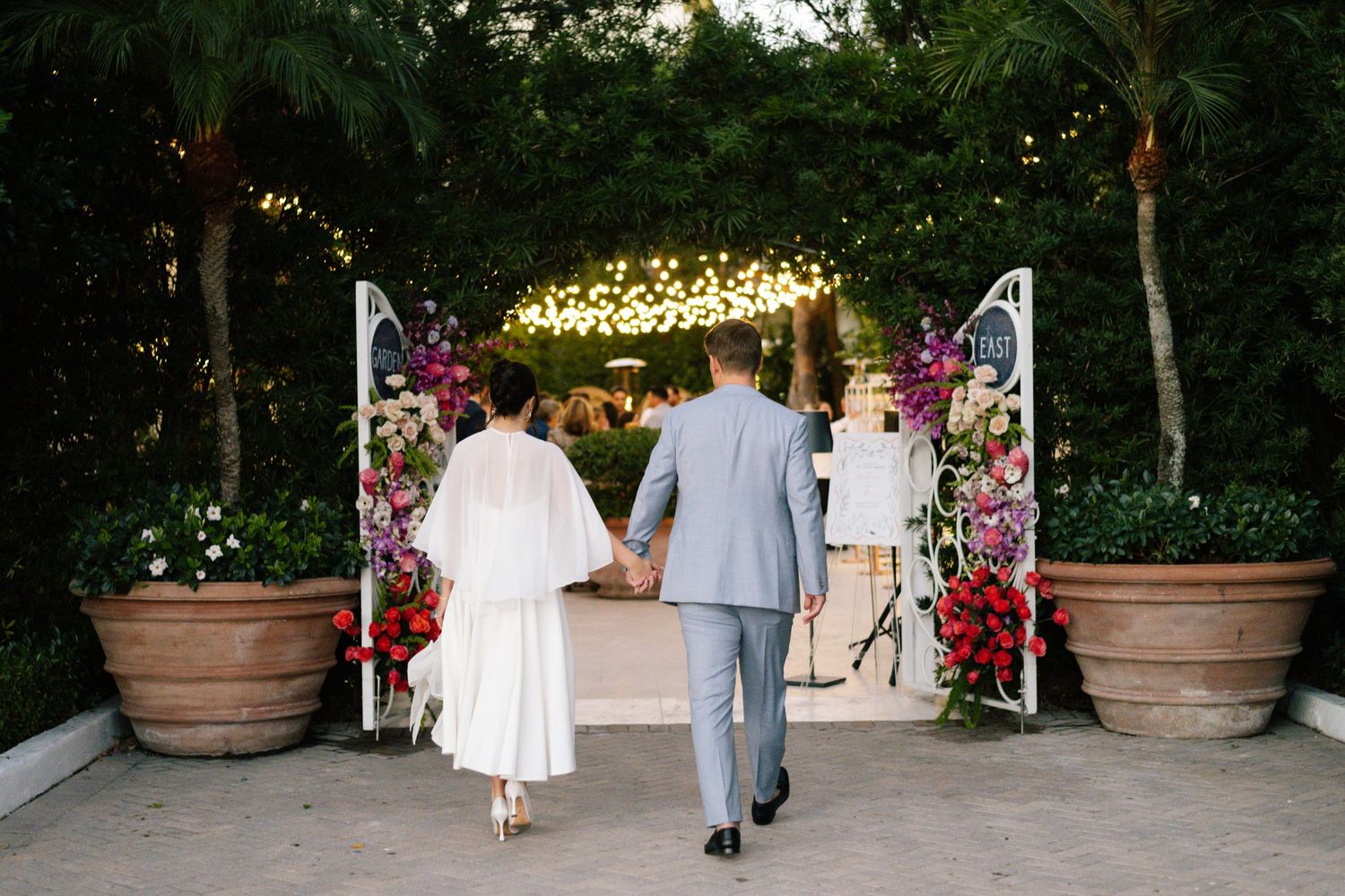 Garden pathway decorated with string lights and floral arrangements for an evening event.