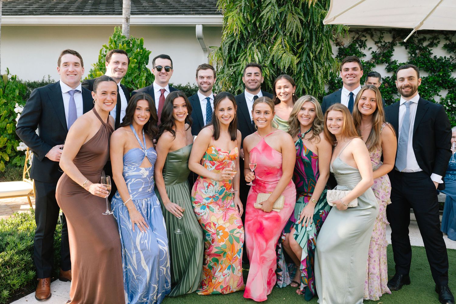 Wedding guests in colorful summer attire gather for outdoor photos.