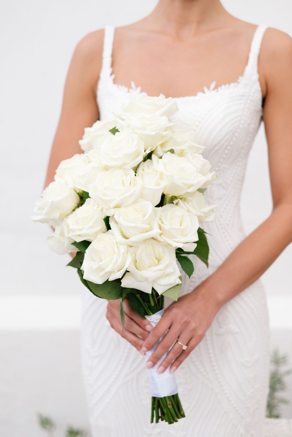 Classic white rose wedding bouquet held against lace wedding dress.