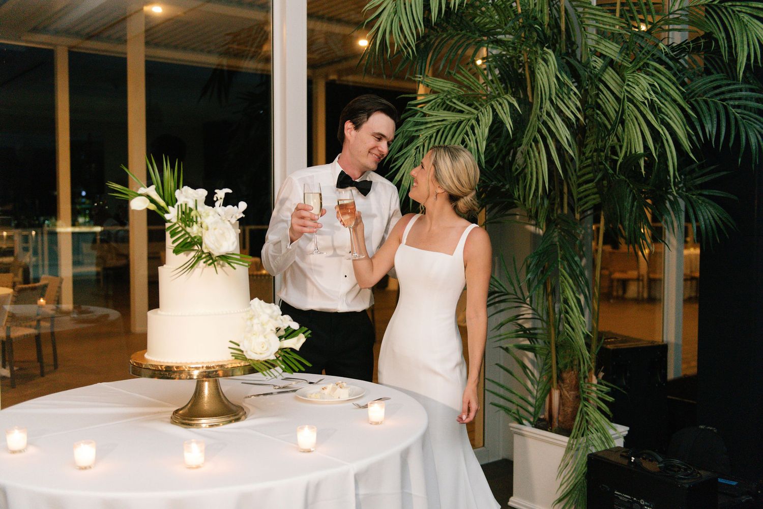 Wedding reception venue decorated with tropical palm plants and ambient lighting.