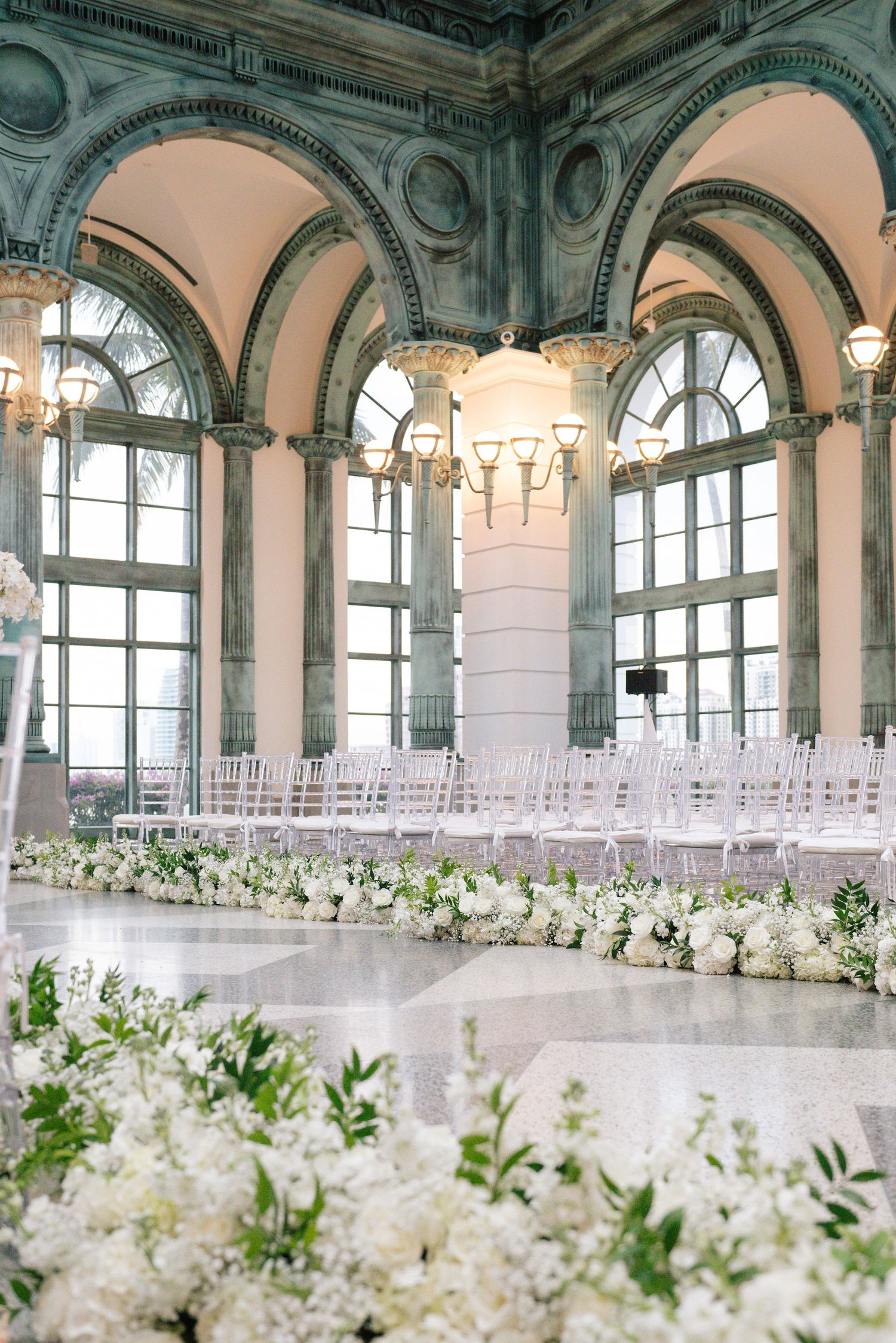Grand ballroom with ornate architecture and white floral aisle decorations for wedding ceremony.