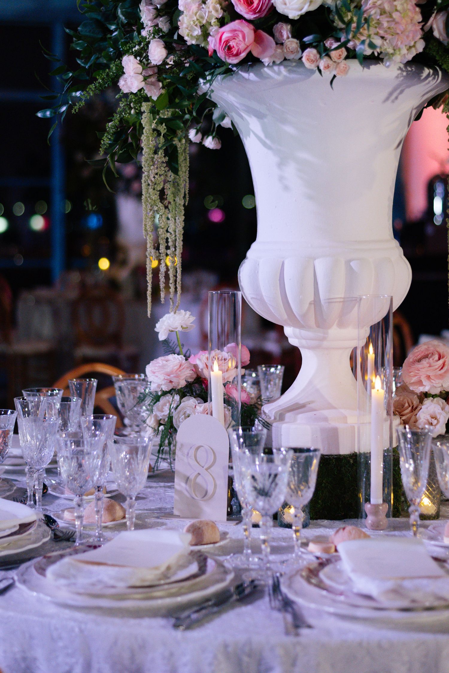 Elegant wedding reception table settings with tall floral centerpieces, crystal glasses, and white linens.