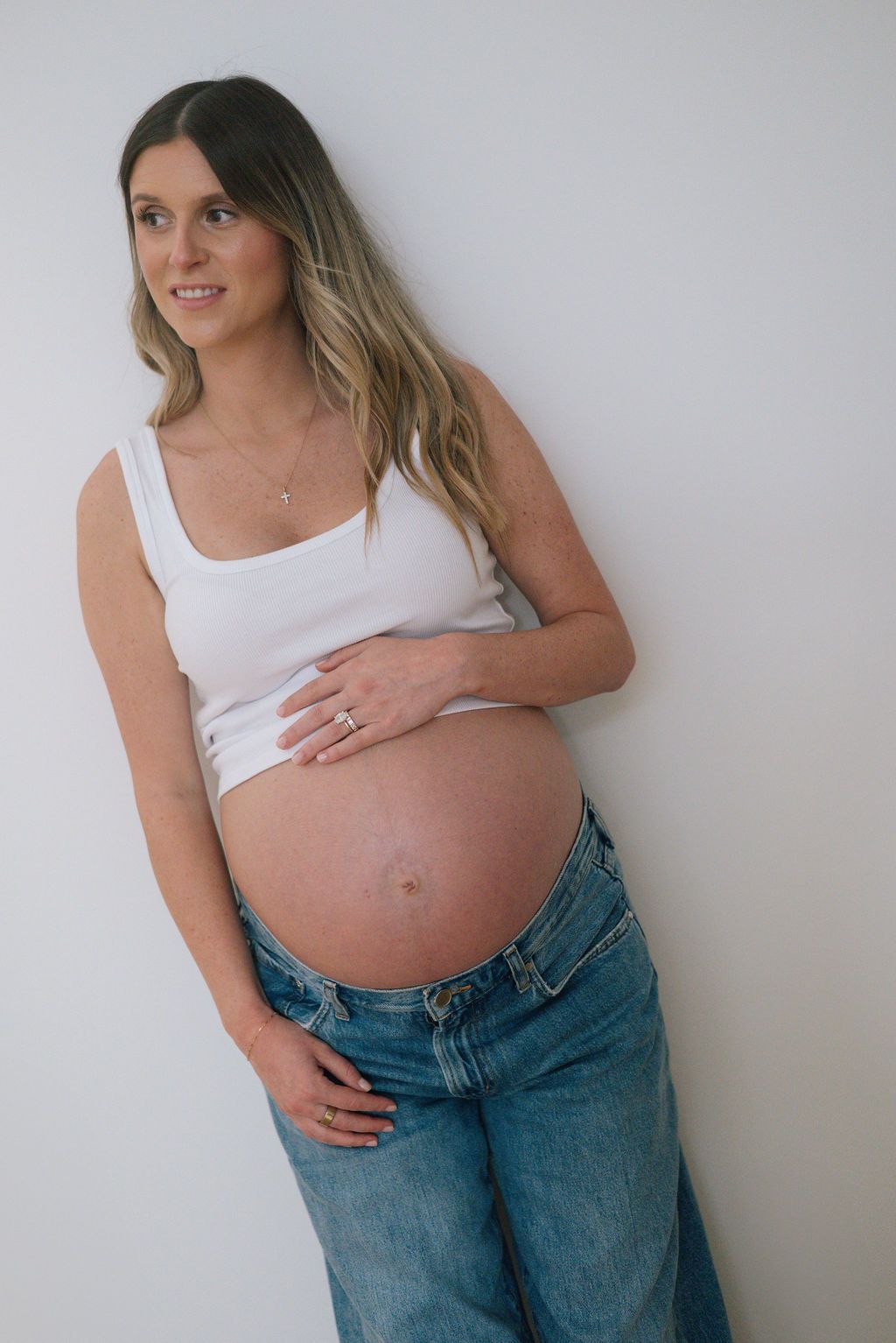 A series of casual maternity poses showing a pregnant belly with jeans and white top.