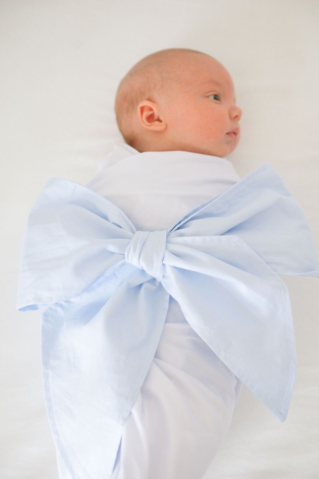 Newborn baby wrapped in white with a large light blue bow.