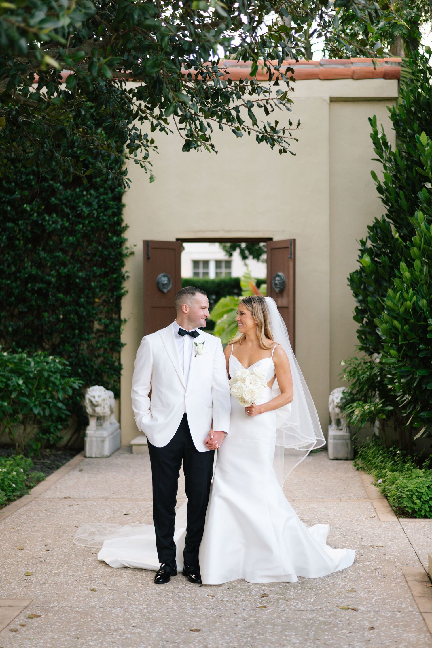 Wedding couple strolling through a garden courtyard with elegant architecture.