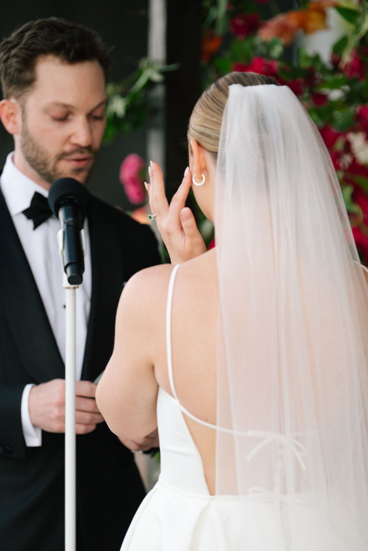 A wedding ceremony moment captured during vows with floral decorations in the background.