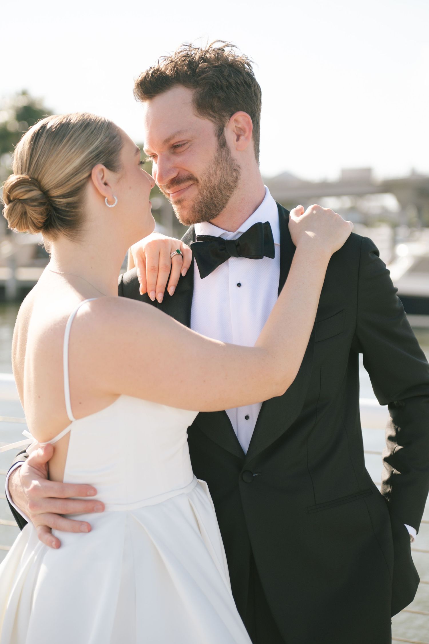 Romantic wedding couple embracing during sunset photoshoot on waterfront.