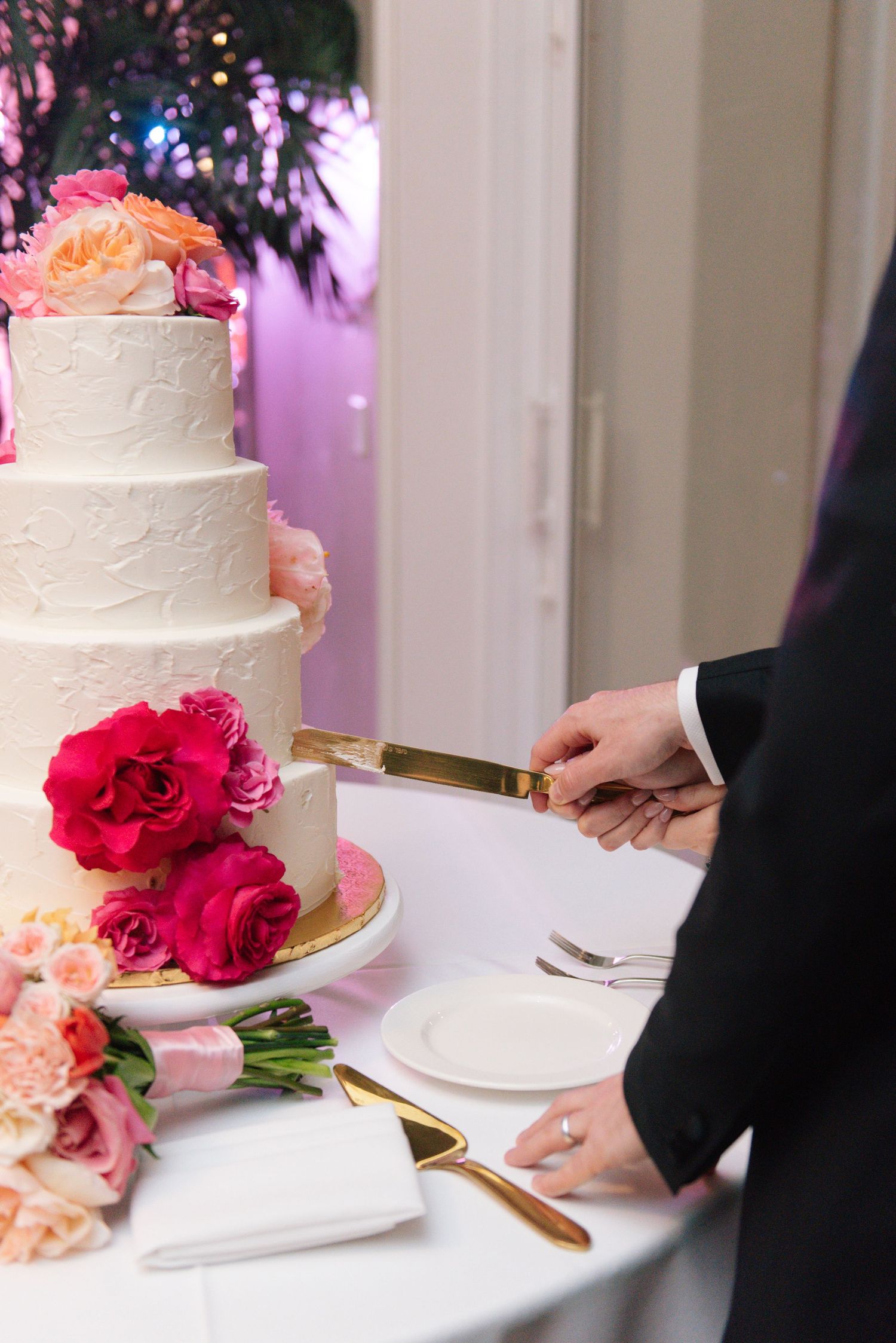 Wedding cake cutting ceremony with elegant white tiered cake adorned with red and pink roses.
