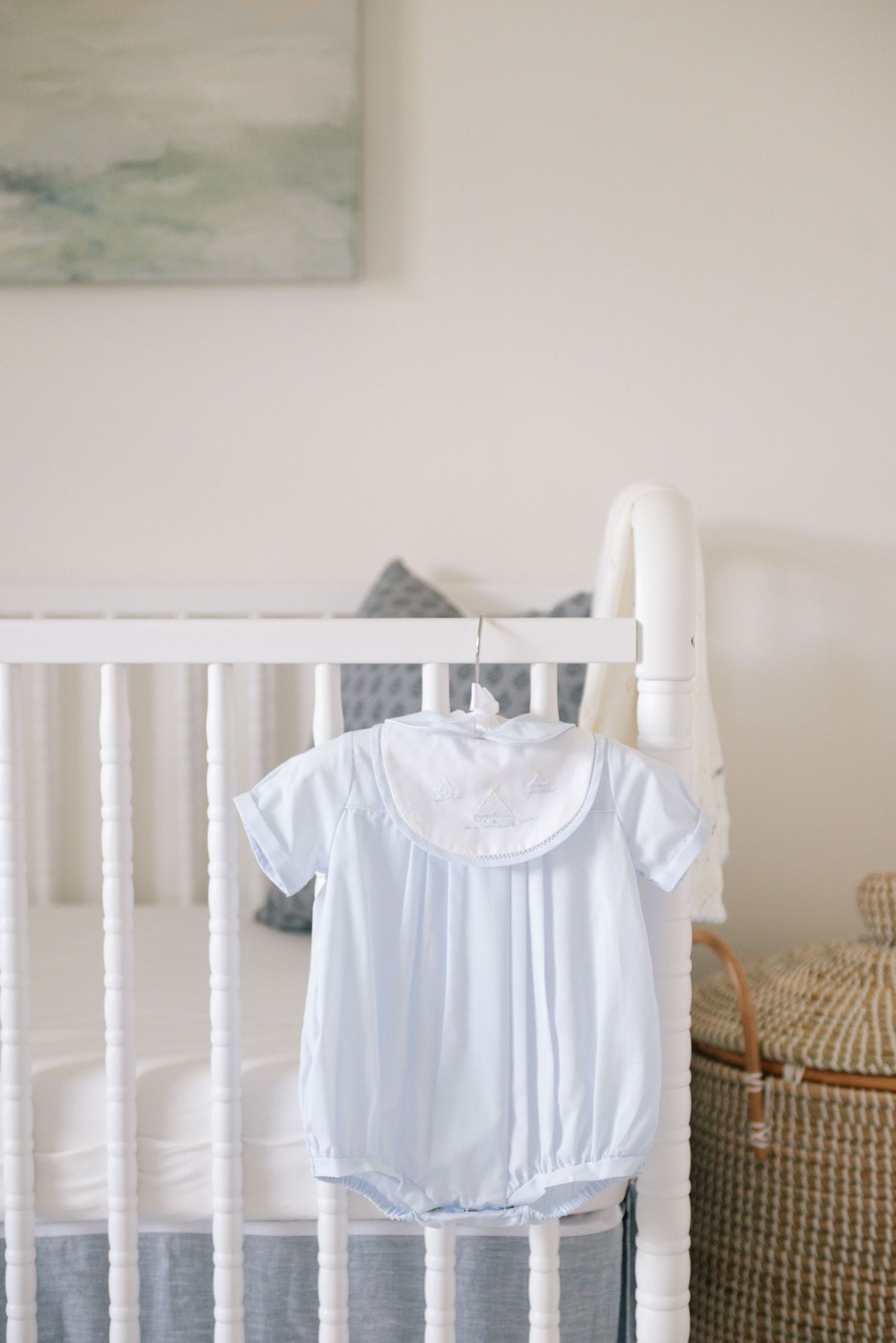 White baby clothes displayed on a white crib rail.