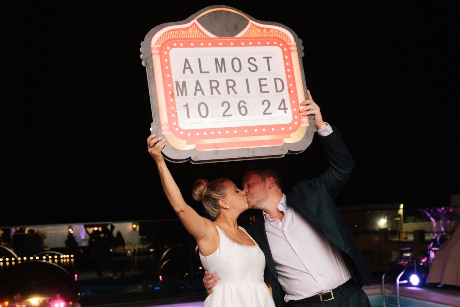 Couple posing with 'Almost Married' sign during nighttime celebration.